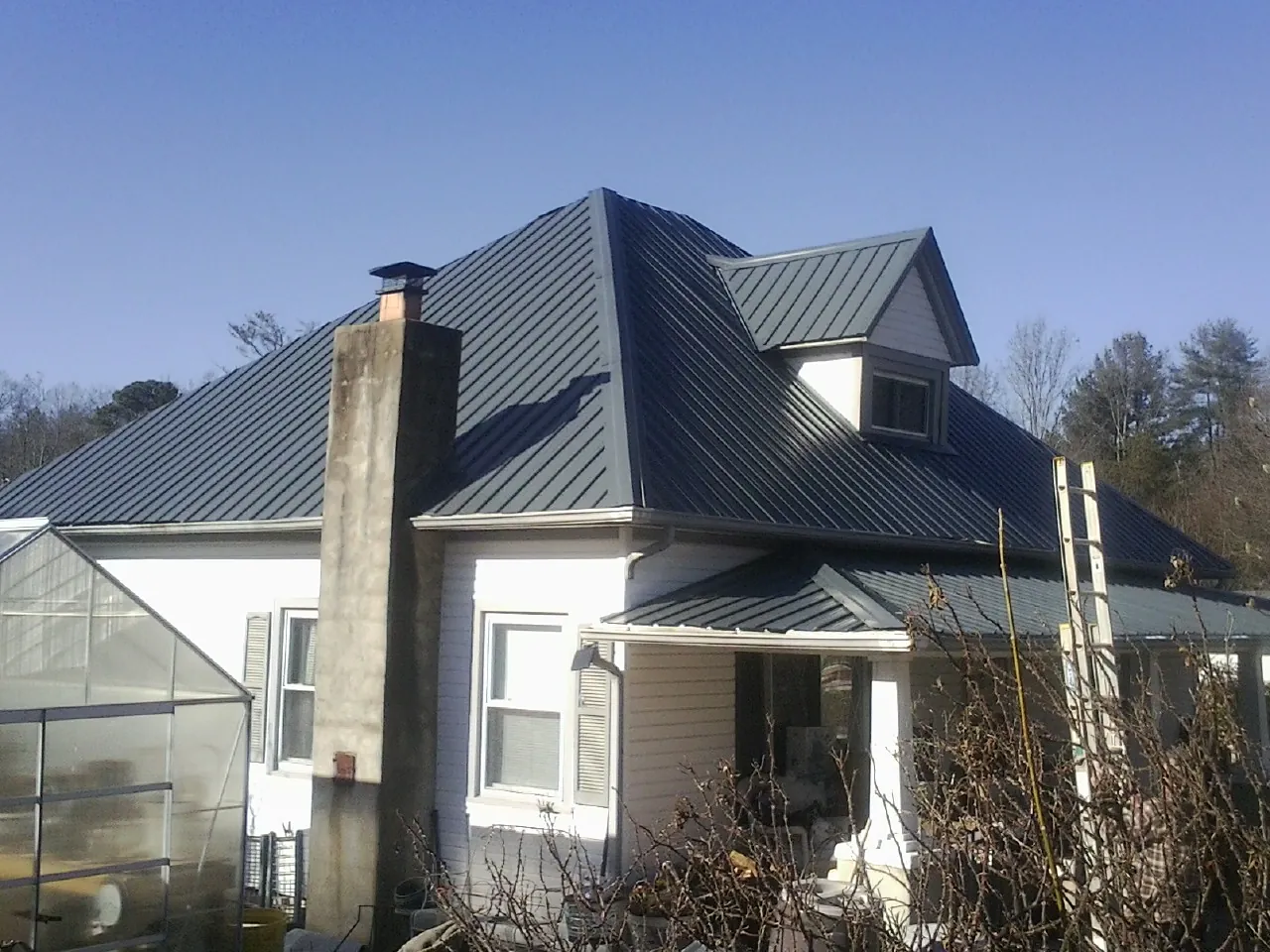 Dark blue standing seam metal roof on a white farmhouse with dormer — Slate & Tile Roof Repair by Roofing Brothers in Safety Harbor