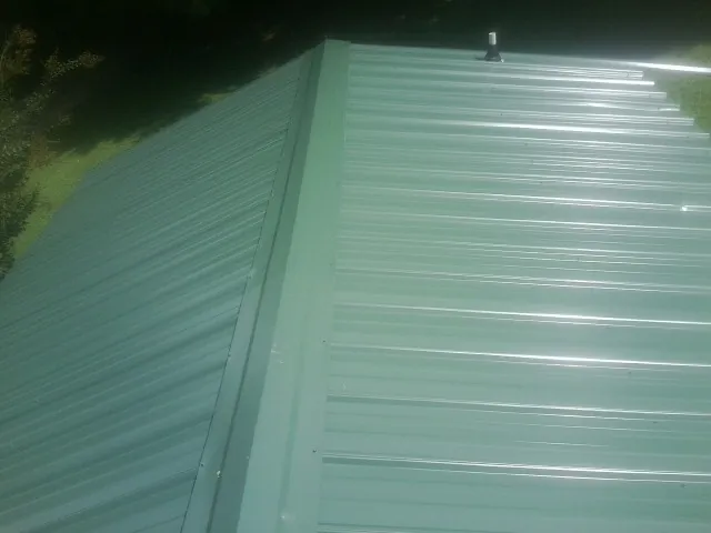 New green metal panels meeting at the ridge of a roof — Flat Roof Repair work by our crew in Safety Harbor