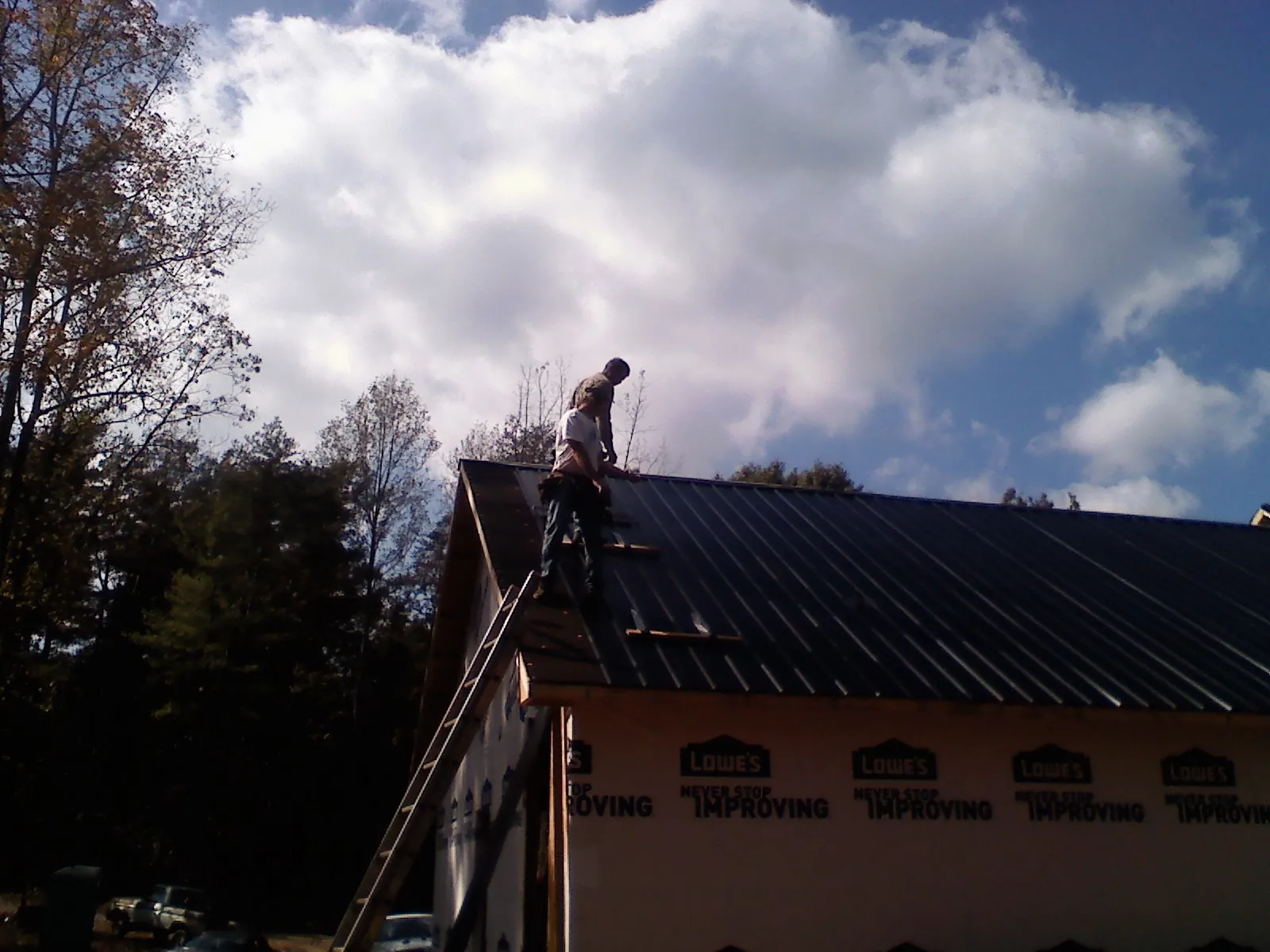 Roofer fastening dark metal panels high against a cloudy sky, from a Roof Inspection job in Safety Harbor