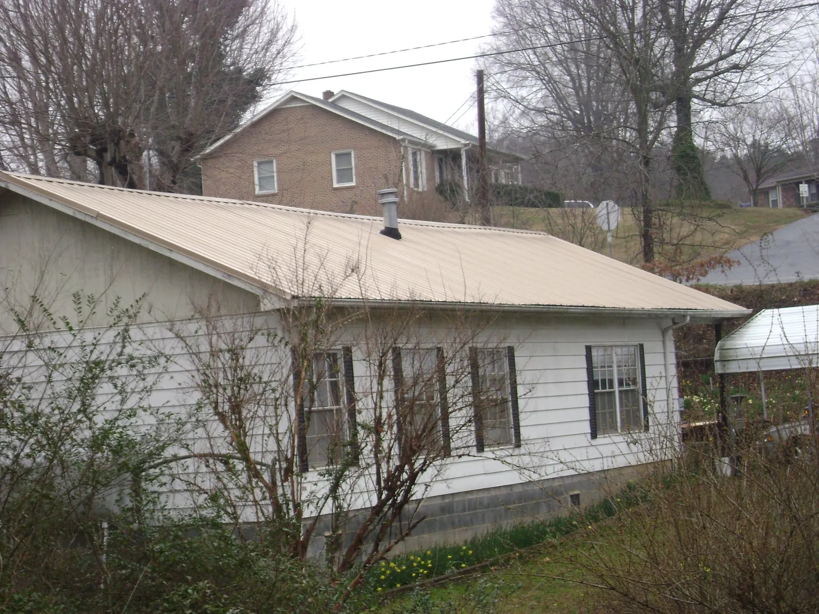 Tan metal roof on a white sided house set into a hillside — Commercial Roofing by Roofing Brothers in Safety Harbor